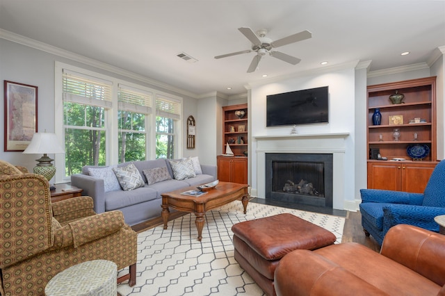 living room featuring ornamental molding, light wood-type flooring, ceiling fan, and built in shelves