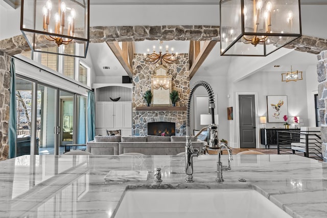 interior space featuring a sink, a high ceiling, a fireplace, stone counters, and a chandelier