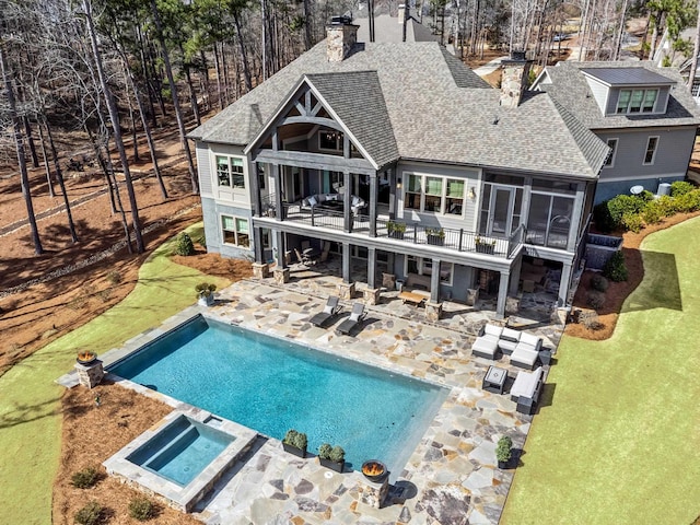 rear view of house featuring a balcony, roof with shingles, an in ground hot tub, a sunroom, and a patio area