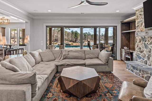 living area with a stone fireplace, wood finished floors, a healthy amount of sunlight, and ornamental molding