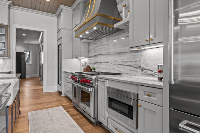 kitchen featuring tasteful backsplash, custom range hood, light stone counters, wood finished floors, and high end appliances