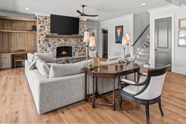 living area with stairs, a fireplace, light wood-type flooring, and ornamental molding