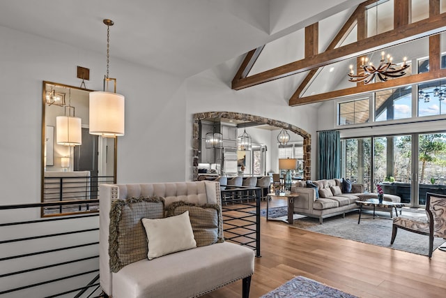 living room featuring light wood-type flooring, beam ceiling, an inviting chandelier, arched walkways, and high vaulted ceiling