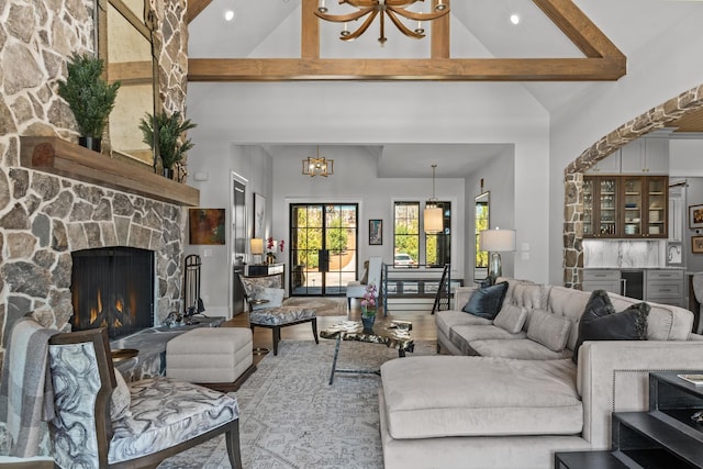 living room with wood finished floors, high vaulted ceiling, beam ceiling, a stone fireplace, and a chandelier