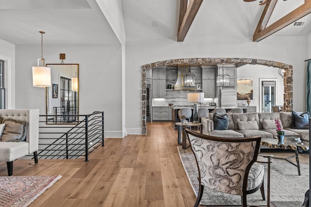 living area featuring visible vents, beam ceiling, high vaulted ceiling, light wood-style flooring, and arched walkways