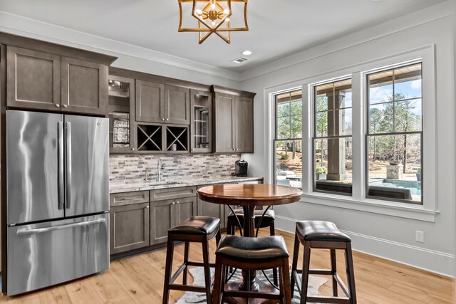 kitchen featuring freestanding refrigerator, a sink, dark brown cabinets, light wood-style floors, and tasteful backsplash