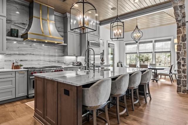 kitchen featuring high end stainless steel range, wall chimney exhaust hood, decorative backsplash, light stone countertops, and wood ceiling