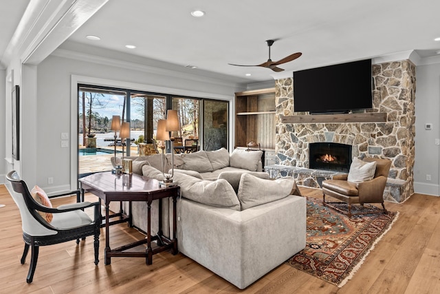 living area featuring ceiling fan, baseboards, ornamental molding, a fireplace, and light wood-style floors