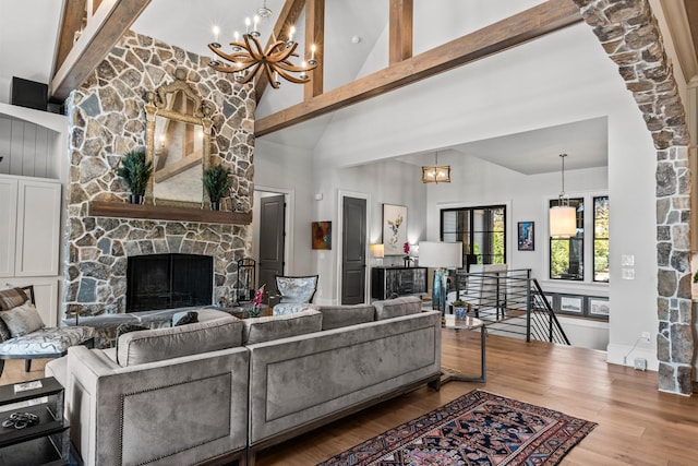 living room featuring beamed ceiling, high vaulted ceiling, wood finished floors, a stone fireplace, and an inviting chandelier