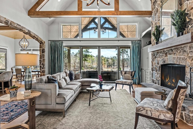 living room with beamed ceiling, a fireplace, high vaulted ceiling, and an inviting chandelier