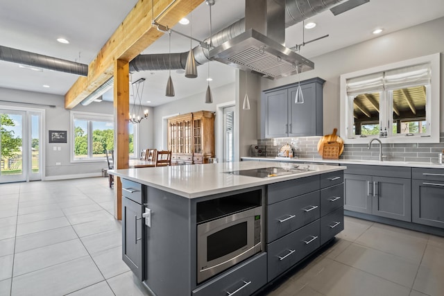 kitchen with gray cabinets, a kitchen island, island range hood, pendant lighting, and stainless steel microwave