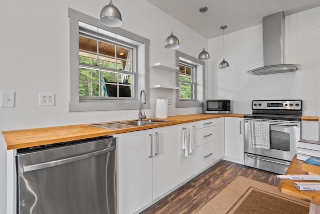 kitchen featuring wall chimney exhaust hood, butcher block countertops, appliances with stainless steel finishes, pendant lighting, and white cabinets