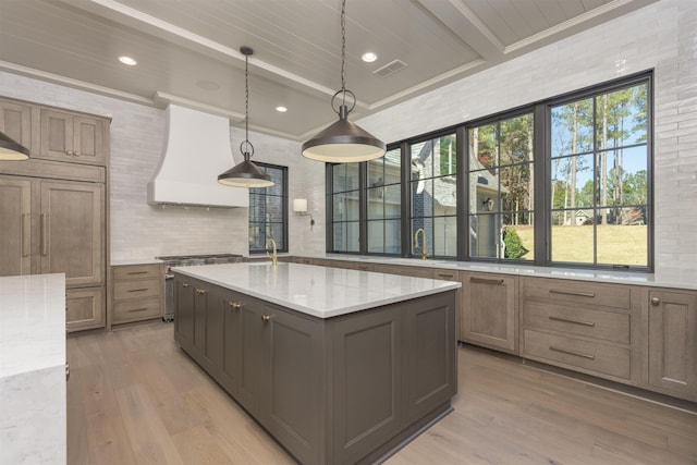 kitchen featuring pendant lighting, custom exhaust hood, light stone countertops, and a center island