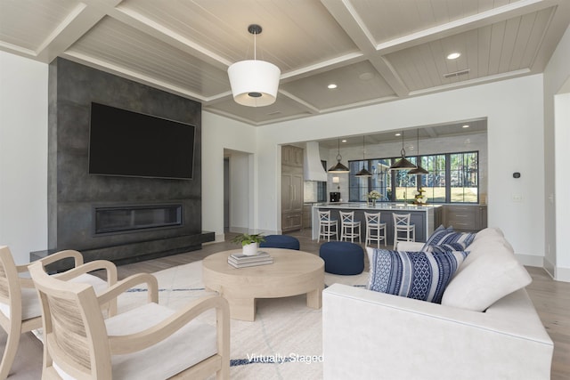 living room featuring beamed ceiling, a large fireplace, wood-type flooring, and coffered ceiling