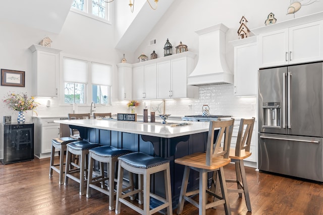 kitchen featuring light countertops, custom range hood, high quality fridge, and a center island with sink