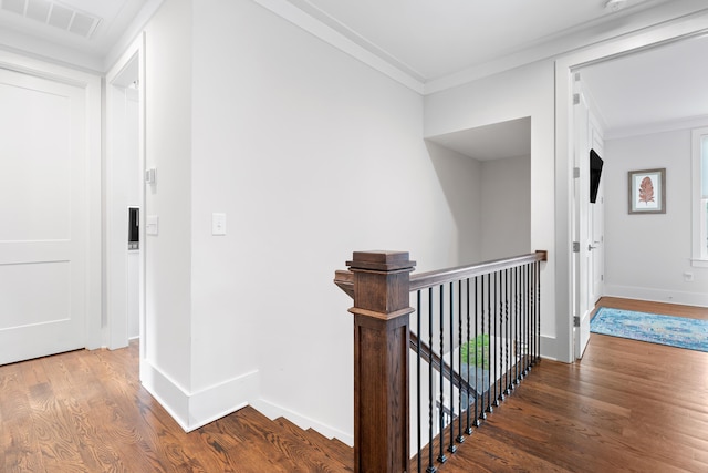 hallway with an upstairs landing, wood finished floors, visible vents, and crown molding