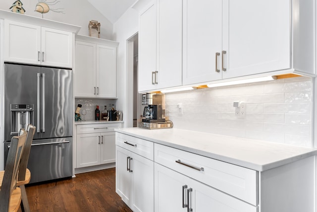 kitchen featuring backsplash, white cabinets, vaulted ceiling, high quality fridge, and light stone countertops