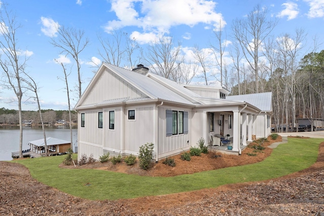 view of property exterior with metal roof, a porch, a water view, a lawn, and a chimney