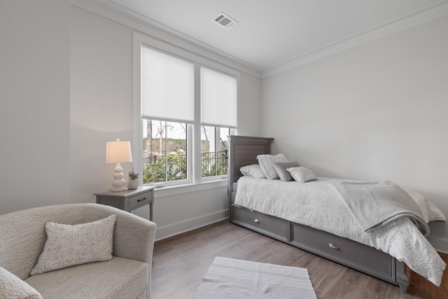 bedroom featuring light wood-style floors, visible vents, crown molding, and baseboards