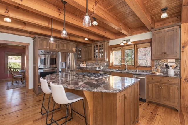 kitchen with dark stone counters, glass insert cabinets, appliances with stainless steel finishes, decorative light fixtures, and a center island