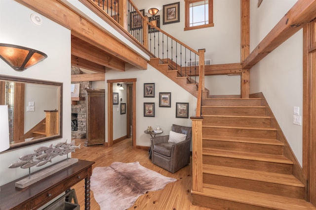 stairway featuring beam ceiling, a towering ceiling, a stone fireplace, wood finished floors, and baseboards