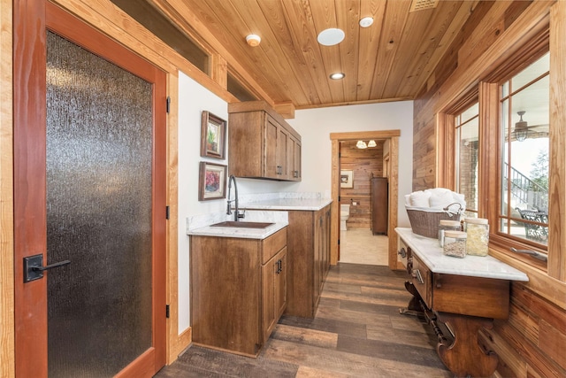 kitchen with wooden ceiling, wood walls, a sink, light countertops, and brown cabinetry