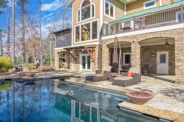 back of property featuring a balcony, stone siding, ceiling fan, and a patio