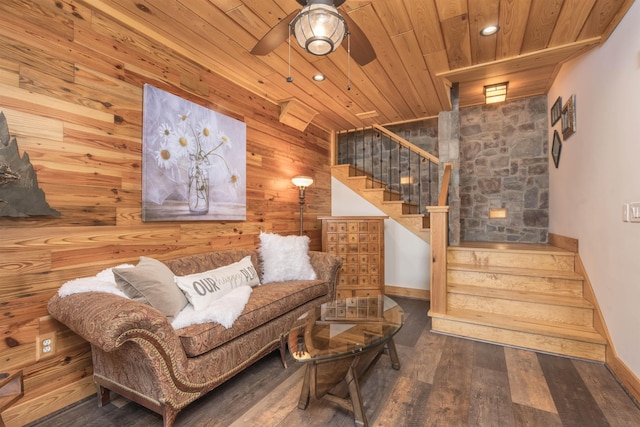 living room featuring wooden ceiling, wood walls, wood finished floors, a ceiling fan, and stairway