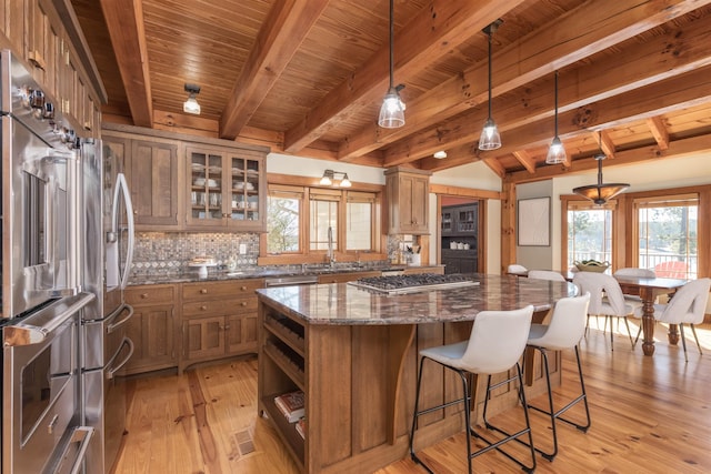 kitchen featuring stainless steel gas cooktop, a kitchen island, dark stone counters, glass insert cabinets, and pendant lighting