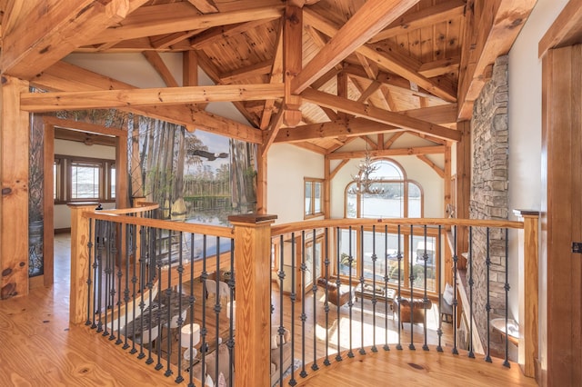 hallway with a chandelier, high vaulted ceiling, an upstairs landing, light wood-style floors, and beam ceiling