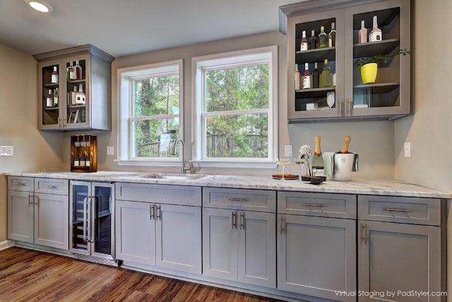 bar with wine cooler, light stone countertops, gray cabinetry, and sink