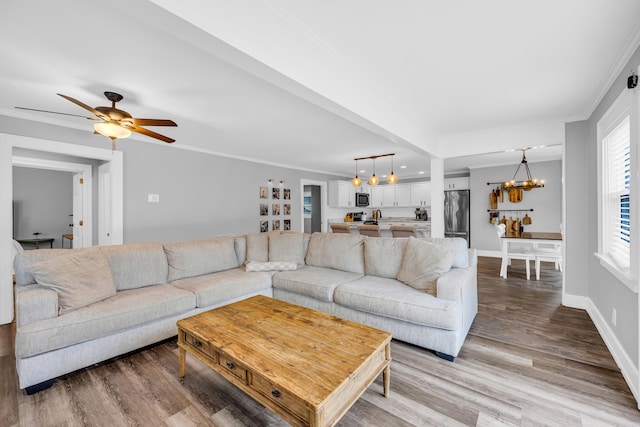 living room featuring hardwood / wood-style flooring, ornamental molding, and ceiling fan with notable chandelier