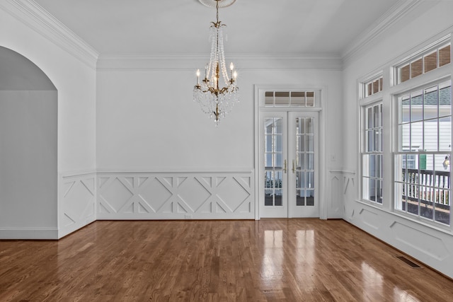 empty room featuring ornamental molding, arched walkways, visible vents, and wood finished floors