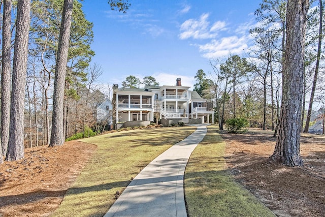 view of front of property featuring a front yard, a sunroom, covered porch, and a chimney