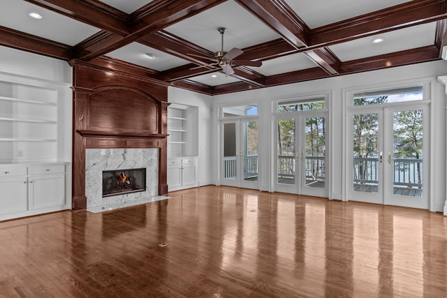 unfurnished living room featuring built in shelves, beam ceiling, plenty of natural light, and a premium fireplace