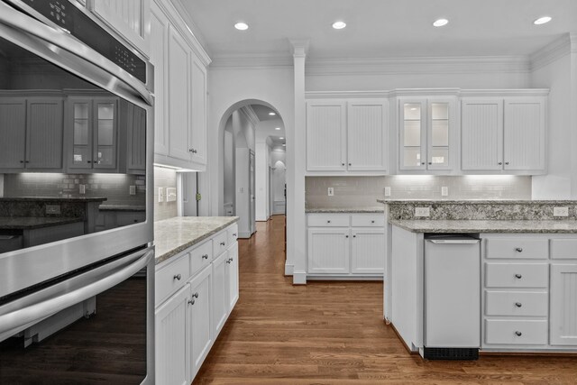 kitchen with arched walkways, double oven, ornamental molding, and white cabinetry