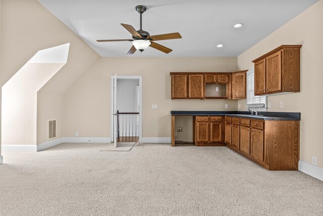 kitchen with brown cabinets, dark countertops, visible vents, a ceiling fan, and light carpet