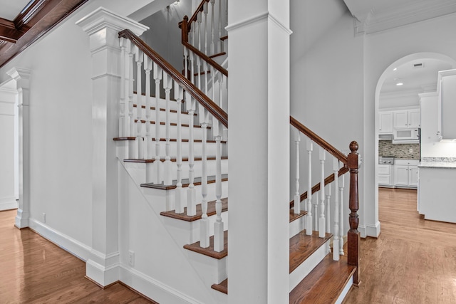 stairs with crown molding, baseboards, arched walkways, and wood finished floors