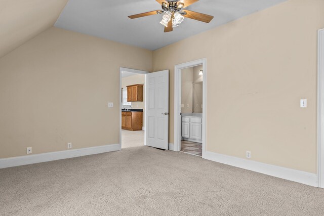 unfurnished bedroom with ceiling fan, lofted ceiling, connected bathroom, light colored carpet, and baseboards