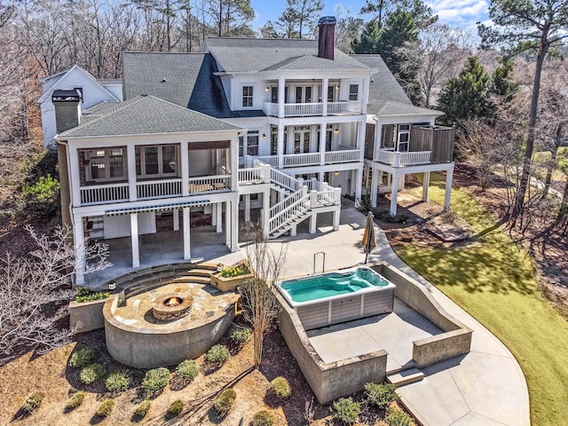 rear view of house with a balcony, a sunroom, a chimney, roof with shingles, and a patio area