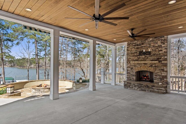 view of patio / terrace featuring a water view, an outdoor fire pit, an outdoor stone fireplace, and ceiling fan