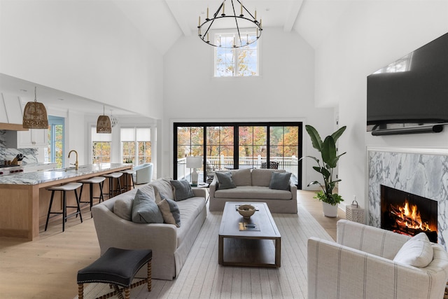 living room with a fireplace, lofted ceiling with beams, sink, a notable chandelier, and light hardwood / wood-style floors