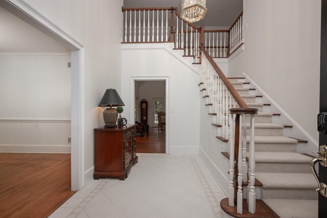 stairs featuring crown molding, a towering ceiling, hardwood / wood-style floors, and an inviting chandelier