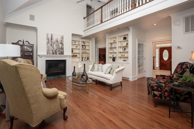 living room featuring built in features, hardwood / wood-style flooring, ornamental molding, a high ceiling, and ceiling fan