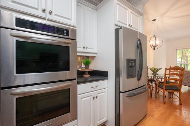 kitchen with crown molding, hanging light fixtures, light hardwood / wood-style flooring, stainless steel appliances, and white cabinets