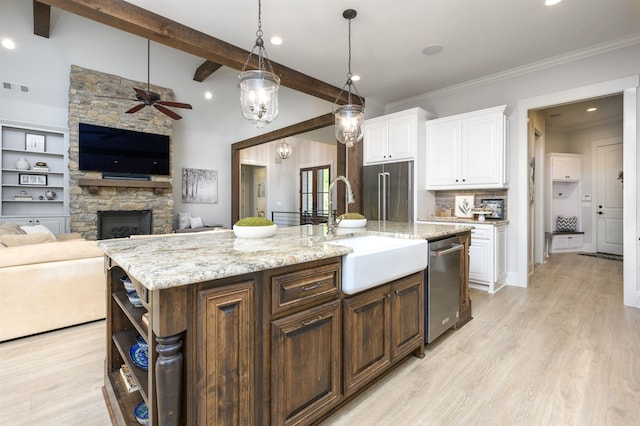 kitchen with appliances with stainless steel finishes, a kitchen island with sink, hanging light fixtures, white cabinetry, and dark brown cabinetry