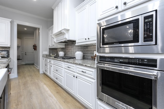 kitchen featuring crown molding, appliances with stainless steel finishes, backsplash, light stone counters, and white cabinets