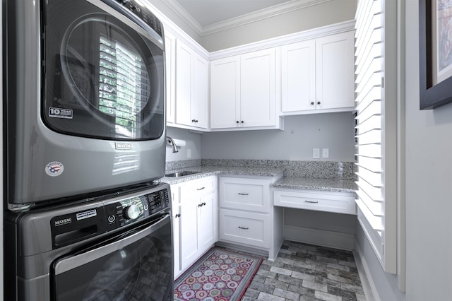 laundry area featuring cabinets, stacked washer and clothes dryer, sink, and ornamental molding