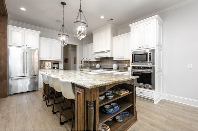 kitchen featuring sink, white cabinetry, stainless steel appliances, light stone countertops, and a center island with sink