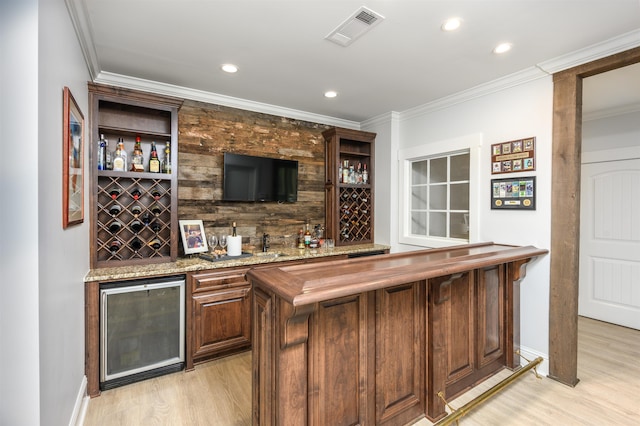 bar with wine cooler, crown molding, light stone countertops, and light hardwood / wood-style floors